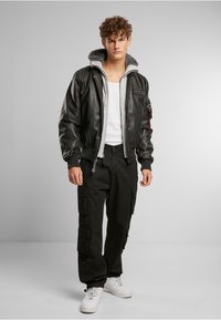 Veste bomber en cuir noir avec doublure en polaire grise, poignets côtelés et fermeture éclair à l'avant. Assortie à un pantalon cargo et des baskets blanches.
