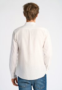 Lichtgekleurde linnen blouse met lange mouwen en een staande kraag. Heeft een rechte zoom en knoopsluiting bij de manchetten. G gedragen met blauwe denim jeans.