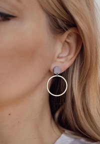 Pendientes de aro de oro con un disco circular mate gris, que presenta una textura suave y un diseño minimalista, colgando del lóbulo de la oreja.