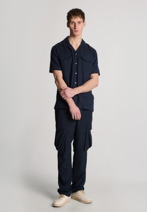 Chemise courte à manches noires foncées avec un col et deux poches poitrine, assortie à un pantalon cargo de la même couleur, avec des poches latérales et une coupe droite.