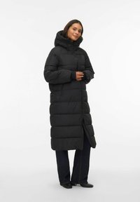 Garš melns pūkainais mētelis ar kapuci, ar rāvējslēdzēju priekšā, ar baffle šuves dizainu un elastīgu aproču nodrošināšanai siltuma un komforta.