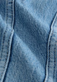 Lichtblau denimstof met een subtiele textuur; heeft contrasterende stiksels langs de randen. De weving is strak en glad.