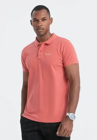 Lyhythihainen polo-paita korallinvärisenä, jossa on tekstuuri viimeistely, kolmen napin lista ja hillitty logotulos rinnassa.