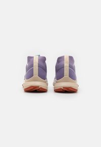 Fioletowe buty sportowe z beżową podeszwą środkową, teksturowanymi akcentami i wyściełanym kołnierzem. Posiadają niebieską pętlę do zakupu oraz gumową podeszwę z czerwoną dekoracją.