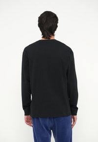 Μαύρο μακρυμάνικο πουκάμισο φτιαγμένο από βαμβάκι, με στρογγυλή λαιμόκοψη και χαλαρή εφαρμογή. Η πίσω όψη επιδεικνύει λεία υφή και απλό σχέδιο.