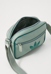 Borsa a tracolla in ecopelle verde con scomparto principale con zip, bordature a contrasto e logo stampato sul fronte. Incluso un manico testurizzato.