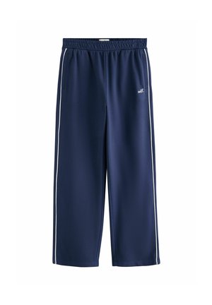 Marineblaue Jogginghose mit weißen Seitenstreifen, elastischem Bund, Taschen und kleinem weißen "self." Schriftzug am oberen linken Bein.