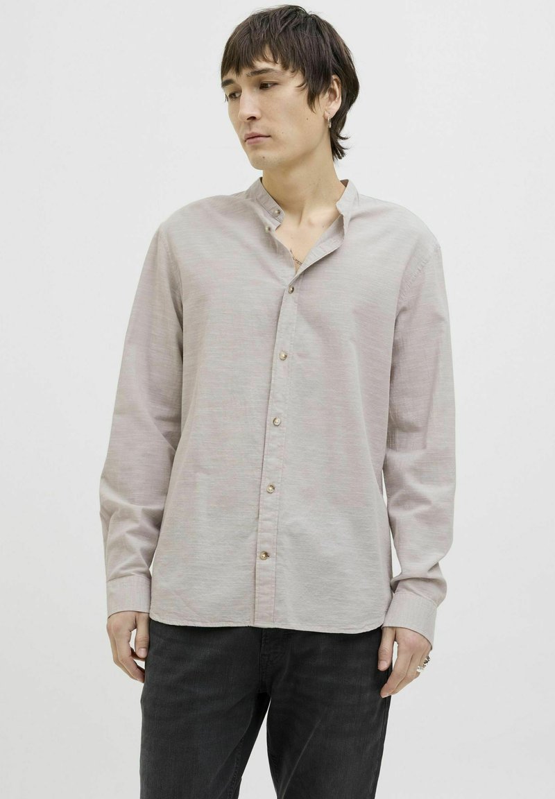 Camisa de color beige claro con cuello mao, de mangas largas y botones visibles. La tela parece suave con una sutil textura.