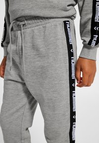 Grå sweatpants med elastisk midja och dragsko, med svarta sidostreck och vit logotext, mjukt bomullsblandat tyg.
