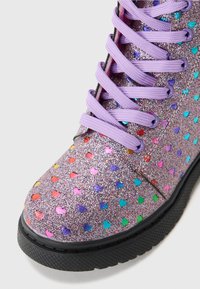 Bottine argentée pailletée avec des motifs en cœurs multicolores, dotée de lacets violets et d'une semelle en caoutchouc noir texturé.