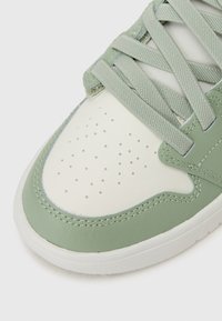 Groene en witte sneaker met een gladlederen bovenwerk, ronde neus, perforaties aan de voorkant en gestructureerde veters. Rubberen zool.