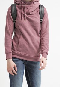 Felpa rosa con cappuccio e collo a imbuto, con lacci, zip laterali e una vestibilità comoda. Abbinate a jeans blu e uno zaino nero.