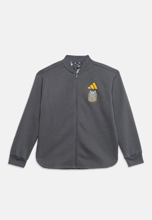 Veste zippée gris foncé avec manches longues, logo Adidas jaune et petit dessin de chien cartoon sur la poitrine gauche.