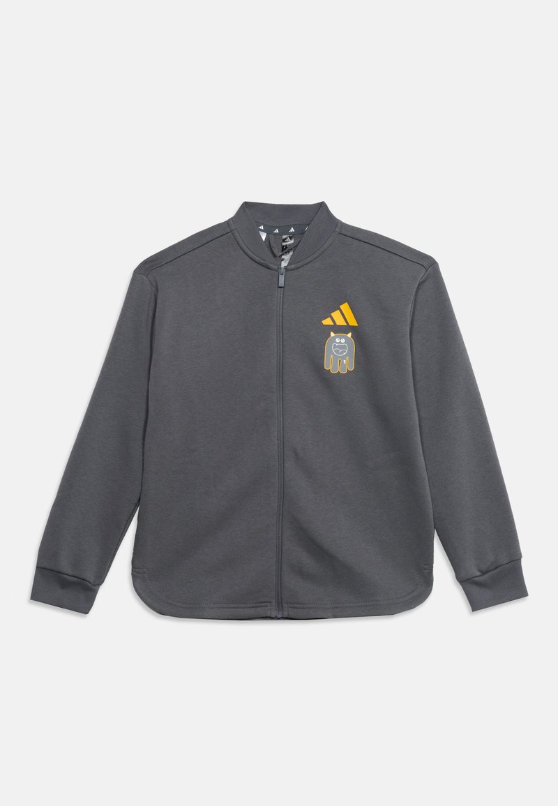 Veste zippée gris foncé avec manches longues, logo Adidas jaune et petit dessin de chien cartoon sur la poitrine gauche.