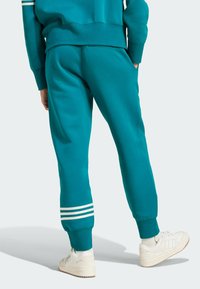 Teal träningsbyxor med vita randiga detaljer vid muddarna, tillverkade i mjukt tyg. Har en avslappnad passform och sidofickor.