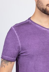 Purple cotton t-shirt with a v-neck, short sleeves, and a slightly textured finish. Features visible stitching and a relaxed fit.