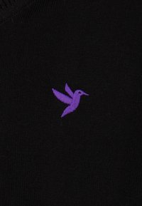 Mustmustri kangas, millel on lilla tikitud kolibri logo. Kujundus rõhutab lihtsaid ja puhtaid jooni ning pehmet tekstuuri.