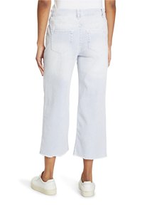 Jean court à rayures bleues et blanches avec ourlet effiloché, dotée d'une taille haute, de poches arrière et d'une coupe décontractée, associée à des chaussures blanches.