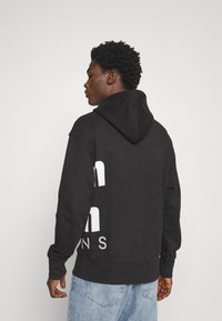 Felpa nera con cappuccio realizzata in tessuto morbido, presentante una grande grafica testuale bianca sul retro, con cappuccio regolabile e polsini a costine.