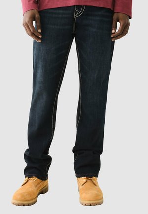 Donkerblauwe denim jeans met contrasterende gele stiksels, rechte pijpen en gedragen met bruine suède laarzen.