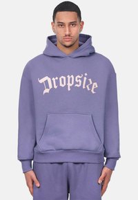 Sudadera morada con bolsillo frontal, con "Dropsie" en una fuente gótica rosa en el pecho. Tela suave, corte relajado, puños acanalados.