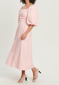 Vaaleanpunainen midi-mekko puffihihoilla ja neliönmuotoisella kaula-aukolla. Mekossa on kerätty yksityiskohtia vartalolla. Yhdistetty valkoisiin remmisandaaleihin.