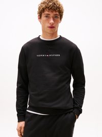 Melna kokvilnas džemperis ar apaļu kakla izgriezumu un ribotām piedurknēm. Priekšpusē ir balta "TOMMY HILFIGER" logo.