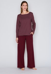 Burgundin värinen pyjama setti, jossa on pitkähihainen toppi venepääntielle ja vaakasuorilla raidoilla, yhdistettynä löysiin, leveälahkeisiin housuihin.