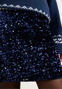 Marineblå paillet mini nederdel med en blank finish, der har et tætsiddende design og en tekstureret overflade af overlapnede runde pailletter.