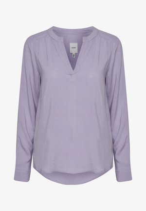 Levandų spalvos ilgio rankovėmis bluzonas su V formos iškirpte, turintis raukšles prie pečių ir apvalų apatinį kraštą. Pagamintas iš lengvos, lygios medžiagos.