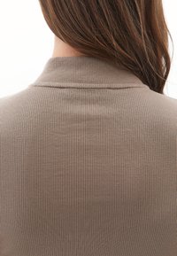 Langt brunt hår, der falder over ryggen på en taupe ribbet turtleneck sweater, set fra bagfra mod en hvid baggrund.