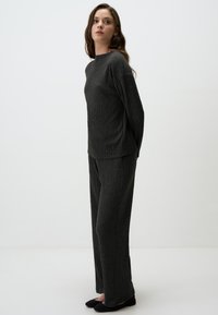 Grijze gebreide loungewear set met een lang mouwtop met een hoge halslijn en een geperforeerde textuur, gecombineerd met rechte broekspijpen. Zwarte ballerina's maken de look compleet.