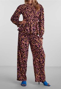 Haut péplum à manches longues à imprimé léopard marron et violet, associé à un pantalon large assorti et des escarpins bleus à bouts ouverts.