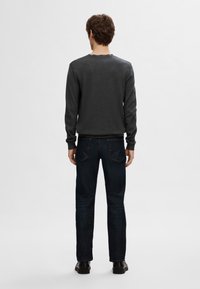 Dark gray sweater with a round neck, paired with dark blue jeans. The fabric appears smooth, and jeans feature back pockets with subtle stitching.