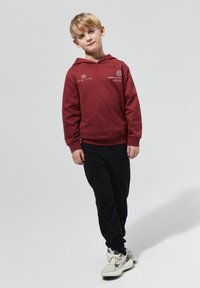 Bordowa bluza z kapturem z przednią kieszenią, szczegóły logo, czarne spodnie dresowe i szare sneakersy z białymi akcentami. Prosty, casualowy projekt stroju.