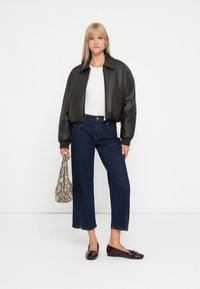 Veste en cuir noir courte, top blanc ajusté, jeans large bleu foncé, ballerines bordeaux foncé et un sac à main en serpent texturé.