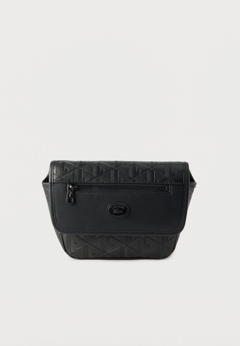 Sac banane en cuir noir embossé avec poche zippée à l'avant et patch logo Lacoste sur un fond uni.