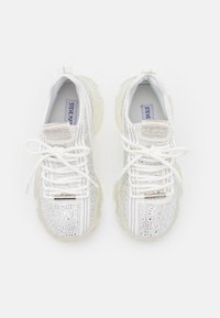 Baskets blanches avec une tige texturée, des accents argentés et des strass, un laçage à l'avant et une semelle en caoutchouc transparent.