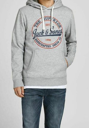 Mann trägt einen hellgrauen Kapuzenpullover mit Fronttasche und "Jack & Jones"-Logo, kombiniert mit blauen Jeans.
