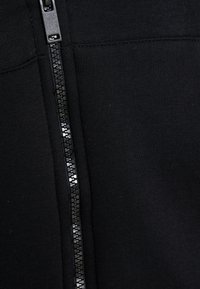 Prenda negra con cremallera que presenta un tejido texturizado con un acabado suave, acentuada por una cremallera brillante en el centro.