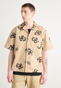 Rövid ujjú, bézs színű pamut ing fekete virágmintával. Gallérral, gombokkal, bal melletti zsebbel és slim fit szabással rendelkezik.