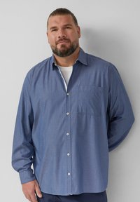 Camicia azzurra con bottoni e tasca, caratterizzata da un piccolo motivo a pois. Maniche lunghe e colletto classico, realizzata in un tessuto leggero.