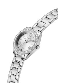 Orologio da polso argentato con numeri romani, lunetta accentuata da cristalli, bracciale a maglie metalliche e cassa tondeggiante. Superficie liscia e riflettente.