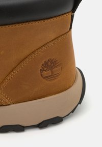 Stivale in pelle marrone con accenti neri, suola crema e cuciture dettagliate. Presenta un logo impresso sul retro.