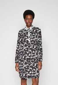 Black and white shirt dress with animal print, featuring long sleeves, a collar, and a buttoned front placket. Smooth fabric texture.