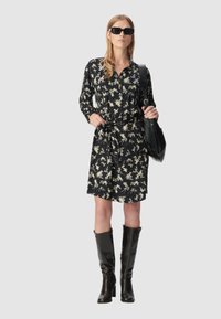 Czarna sukienka w kwiaty z długimi rękawami i wiązaniem w talii, zestawiona z wysokimi na kolana czarnymi kozaczkami i ciemnymi okularami przeciwsłonecznymi. Gładki materiał o błyszczącym wykończeniu.