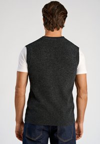 Mörkgrå stickad ärmlös tröja med ribbad halsringning och fåll, lagd över en vit kortärmad skjorta, vilket visar upp en slät textur.