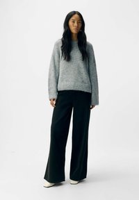 Grauer gestrickter Pullover mit langen Ärmeln, lockerer Passform. Kombiniert mit schwarzen weit geschnittenen Hosen und weißen Ankle Boots. Einfaches und strukturiertes Design.