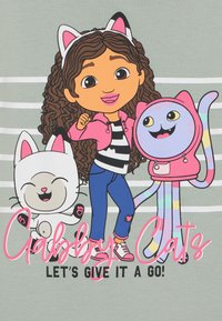Desenho animado com uma rapariga de cabelo castanho encaracolado, vestindo uma jaqueta rosa e uma camisa às riscas, ao lado de um gato branco sorridente e de um polvo colorido.