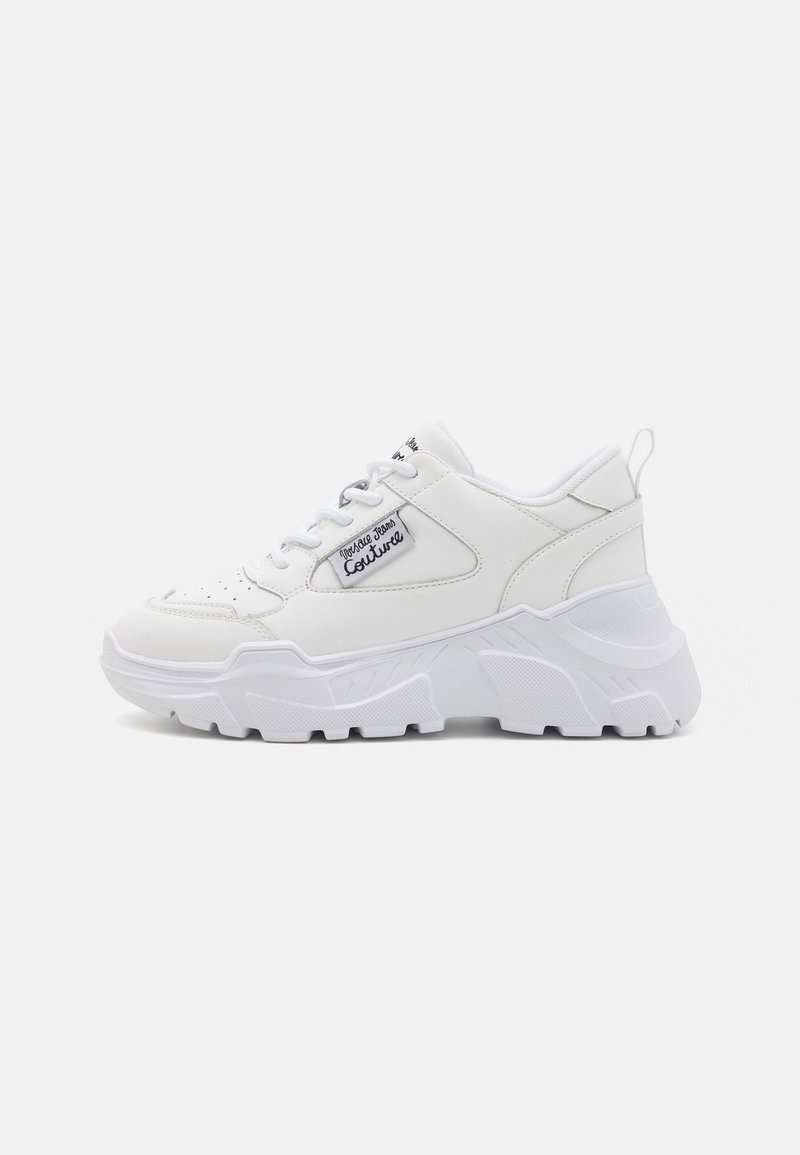 Baskets épaisses blanches avec semelle texturée épaisse, fermeture à lacets à l'avant, et écusson de marque sur le côté indiquant "Vosture Jeans Couture."